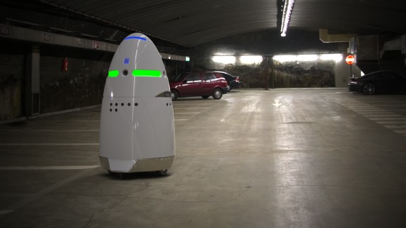 A Knightscope K5 robot patrols an empty parking lot.