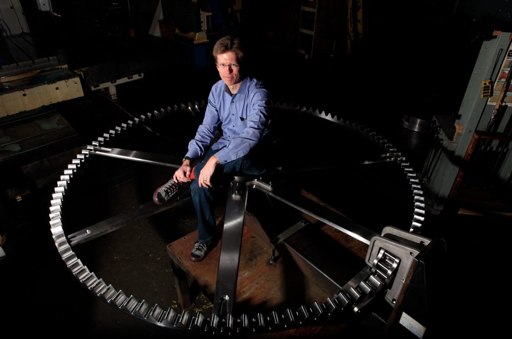 photo of Dylan in a blue shirt, sitting on a giant metal gear, looking up at the camera