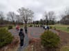 Photograph of people walking a labyrinth laid out in brick and gravel in a field, among bare trees, under an overcast sky.