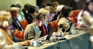 Photo showing three writers working at laptop computers in the middle of a group of people at a conference