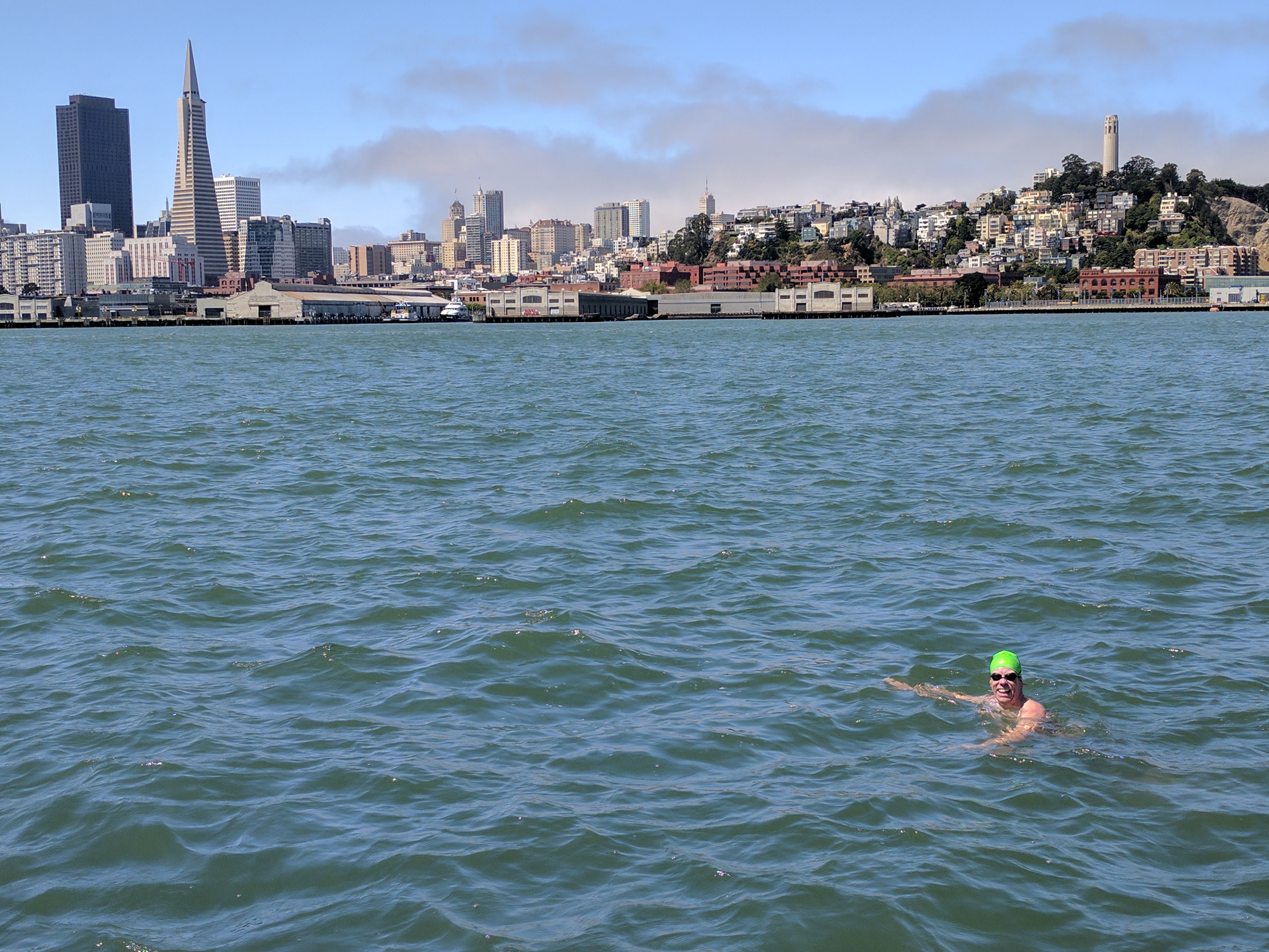 A swimmer in the water with the San Francisco skyline, Transamerica Pyramid on the left and Coit Tower on the right.