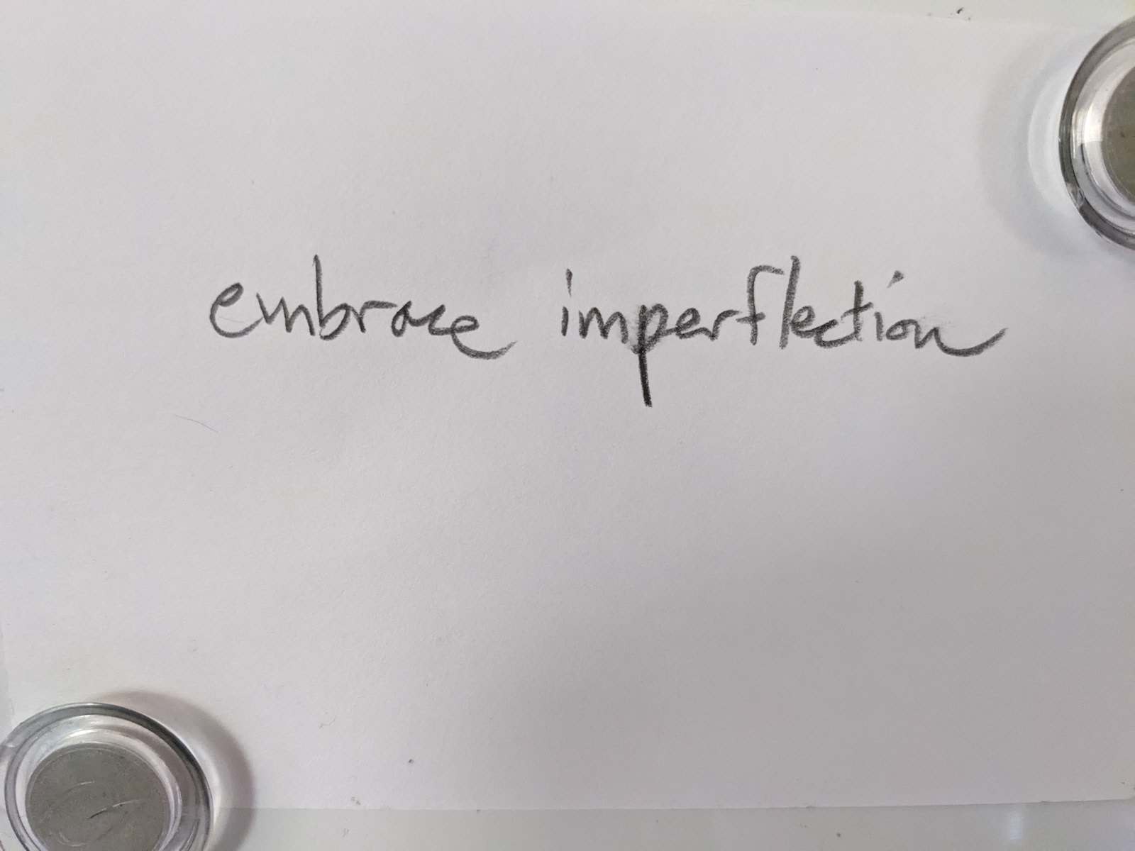 handwriting on a card held up by fridge magnets. text of the writing says "embrace imperflection"